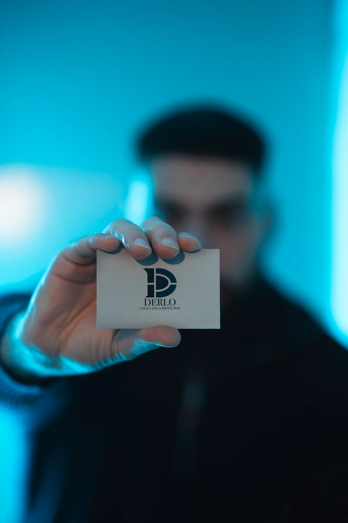 A hand holds a DERLO business card in sharp focus in front of a blurred person.