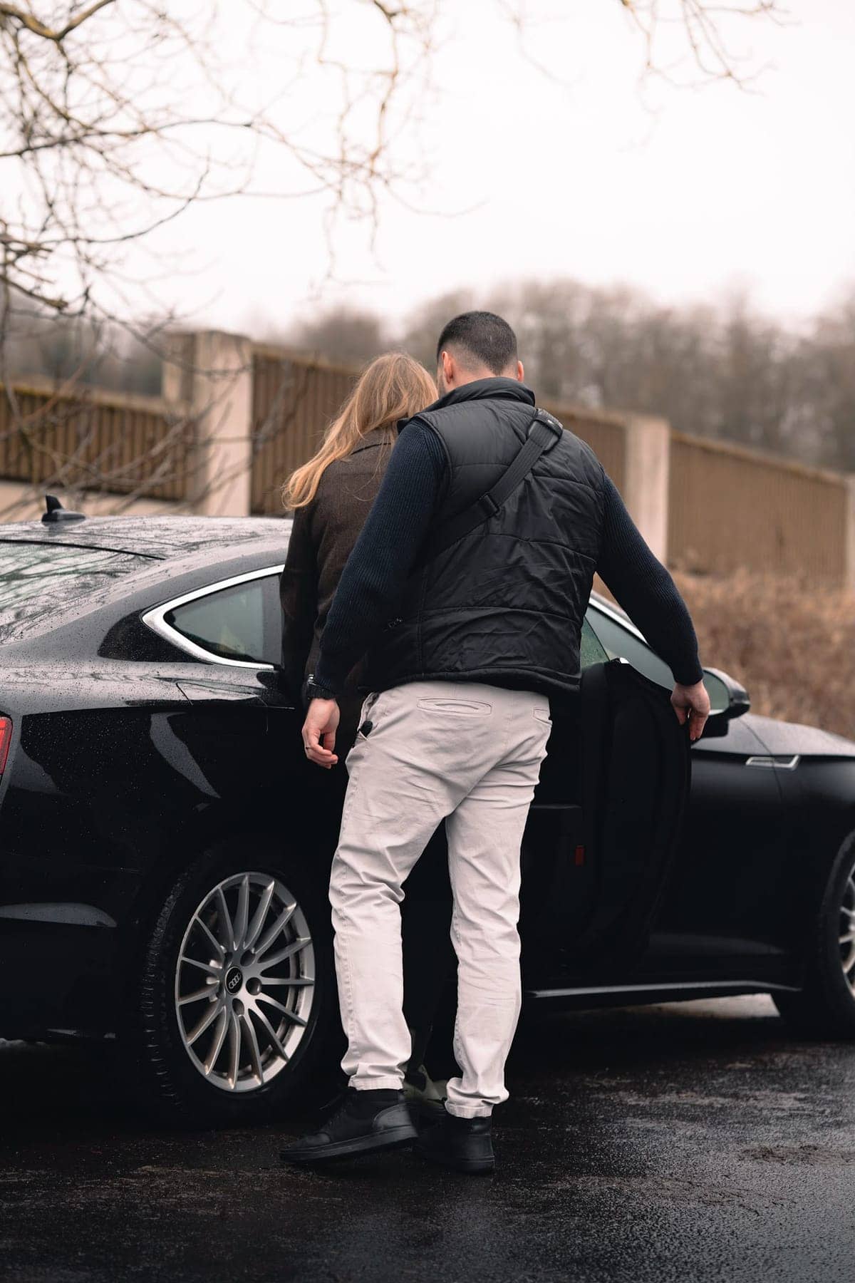 Ein Personenschützer hält einer Frau die Tür einer schwarzen Limousine auf; beide sind von hinten zu sehen.