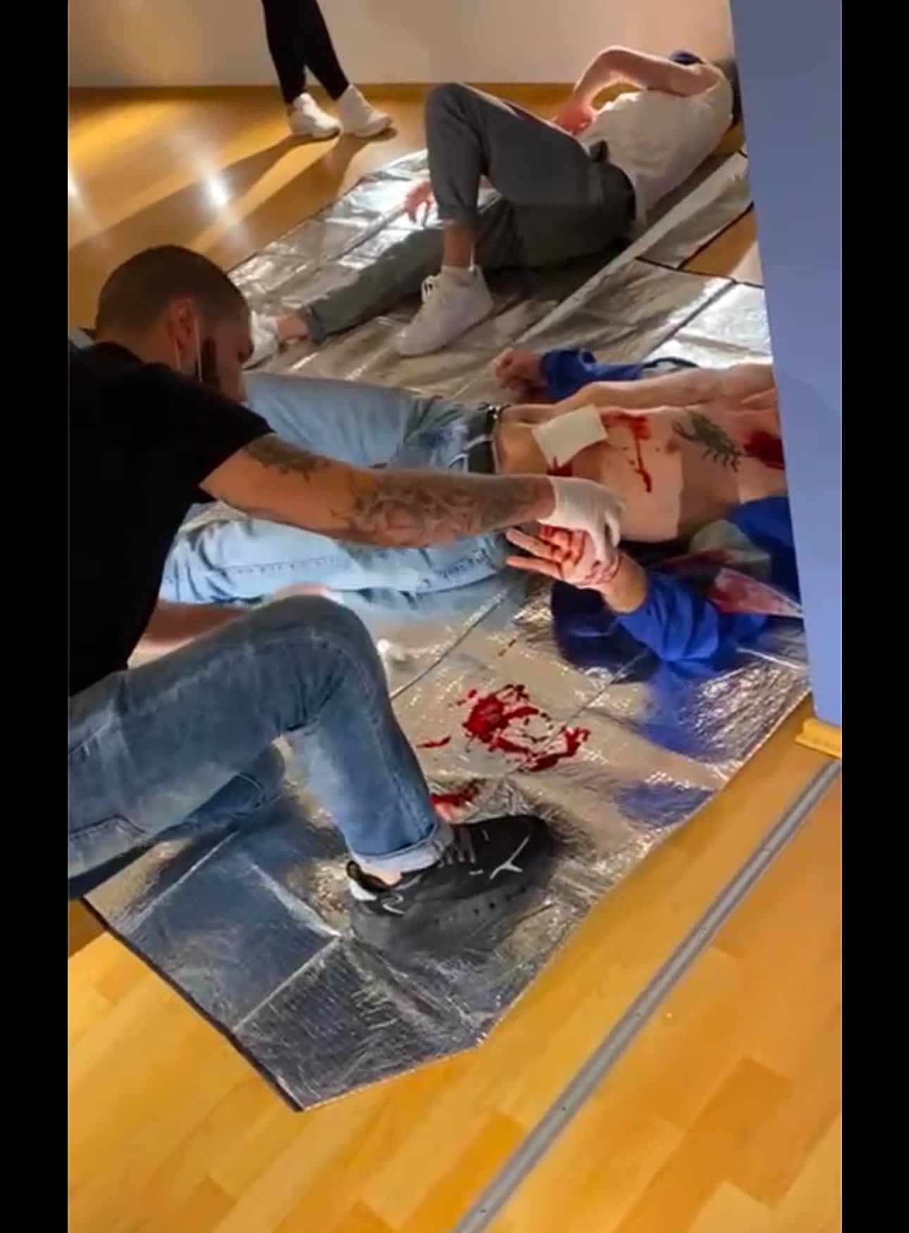 Übung zur Erstversorgung: Mit Einmalhandschuhen wird eine dargestellte Verletzung bei einer Person versorgt, die auf einer Rettungsdecke am Boden liegt.