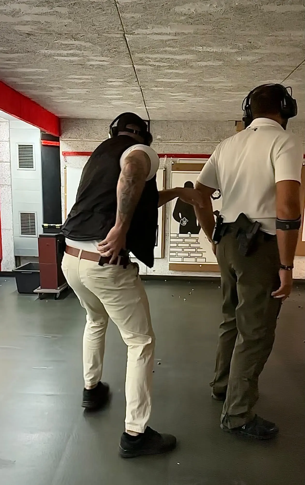 Schießtraining auf einem Schießstand: Zwei Männer mit Gehörschutz stehen vor den Zielscheiben, einer hat die Hand am Holster.