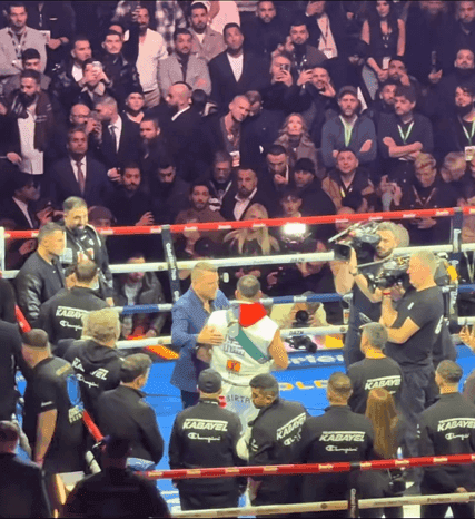Ring area at a boxing event: people in and around the ring, with densely packed rows of spectators behind.