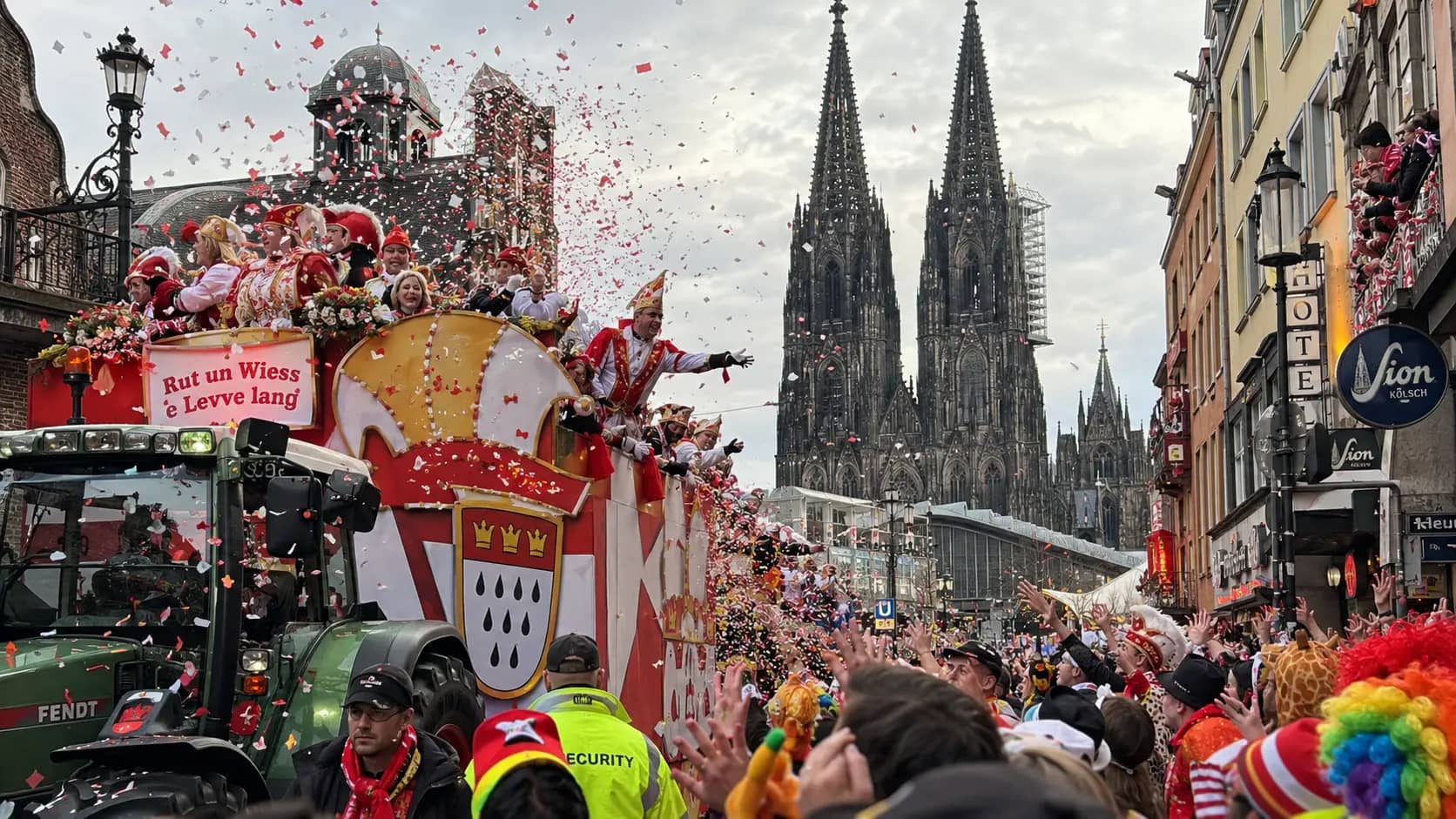 Carnival parade in front of Cologne Cathedral with floats, confetti, spectators and security staff beside the float