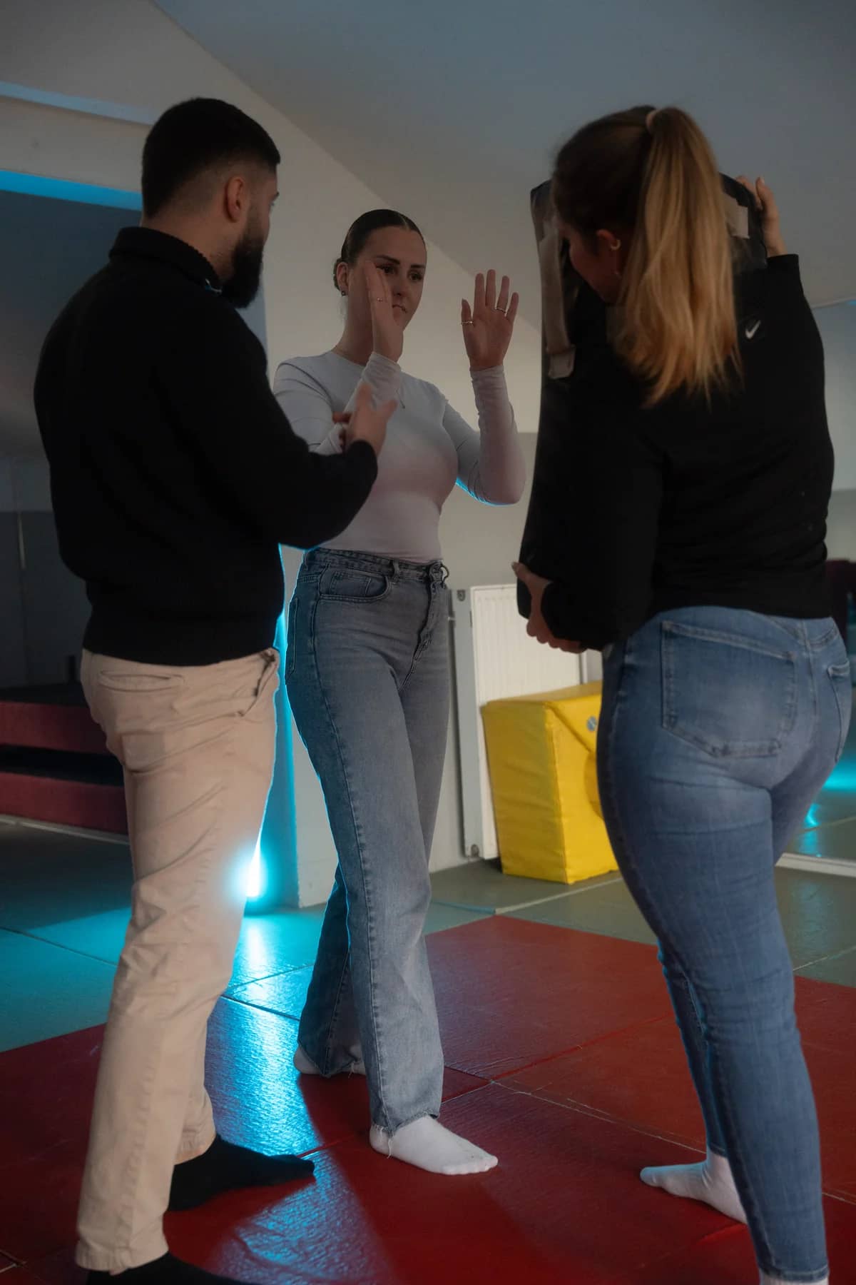 Ein Ausbilder erläutert zwei Teilnehmerinnen eine Selbstverteidigungsübung auf Trainingsmatten.