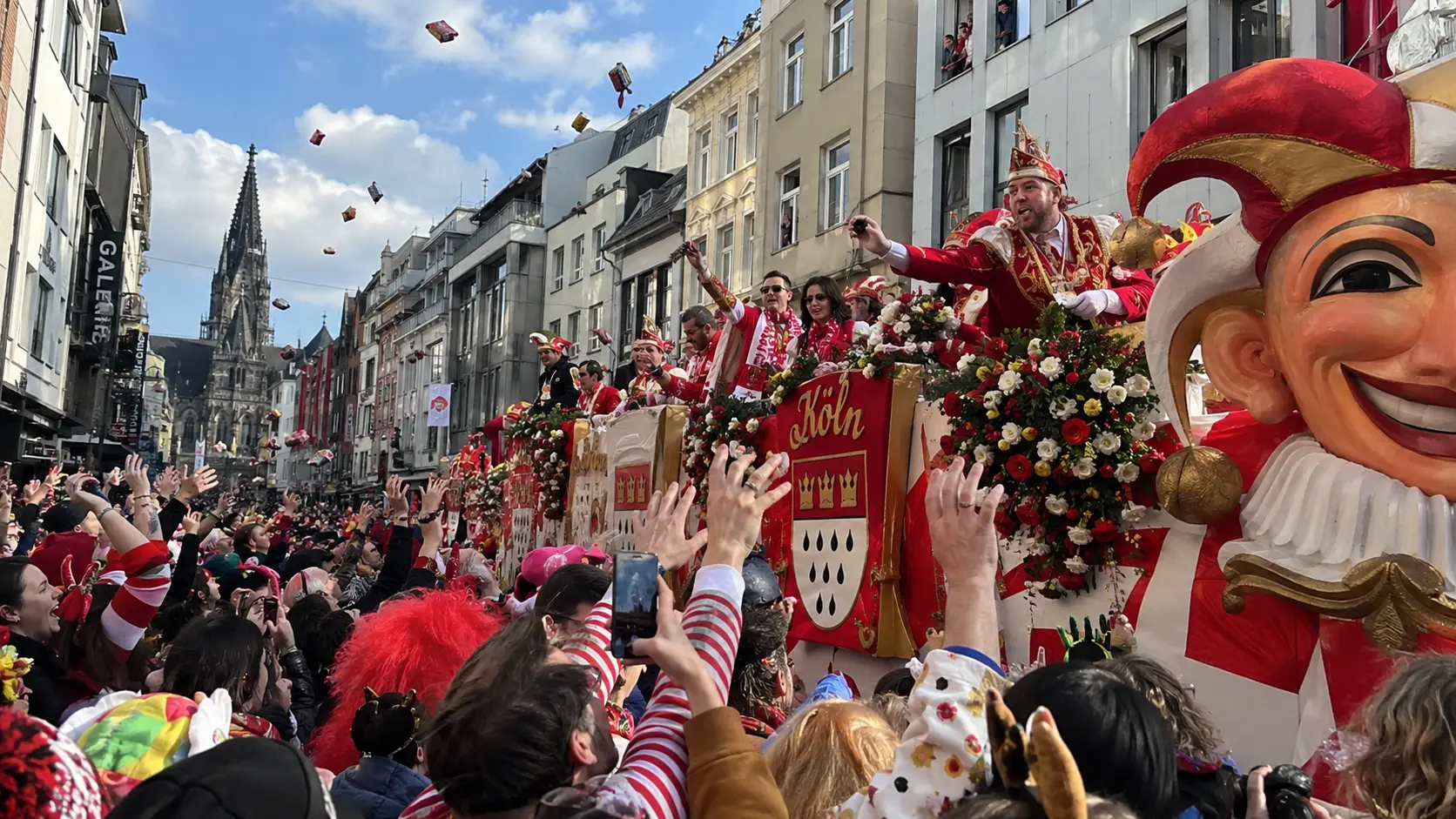 Carnival float with a large jester figure in a Cologne street, crowds celebrating in front