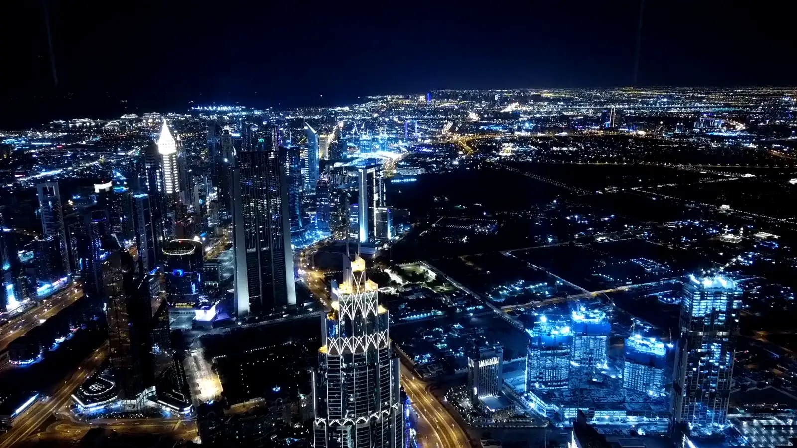 Nächtlicher Blick von oben auf beleuchtete Hochhäuser und Straßen in Dubai, die Lichter der Stadt reichen bis zum Horizont.