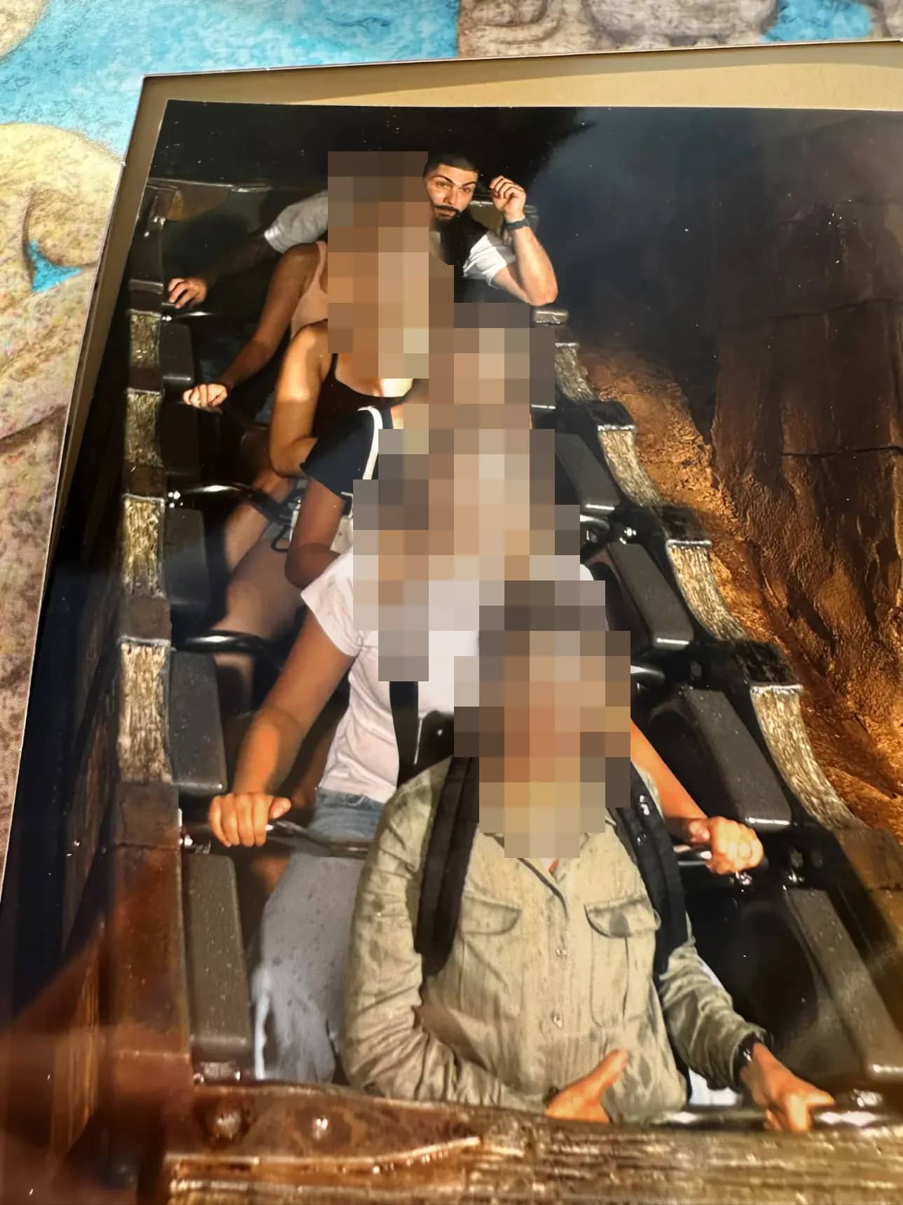 Souvenir photo from a theme park ride: several people sit one behind the other in the car, the faces of the passengers in front of the man in the back row are pixelated.