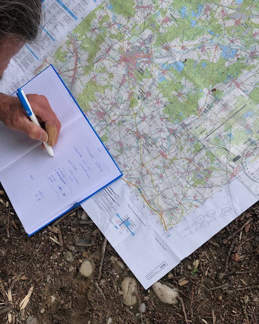 Vorbereitung mit Karte: Eine Hand schreibt Notizen in ein Notizbuch, daneben liegt eine aufgefaltete Landkarte auf dem Boden.