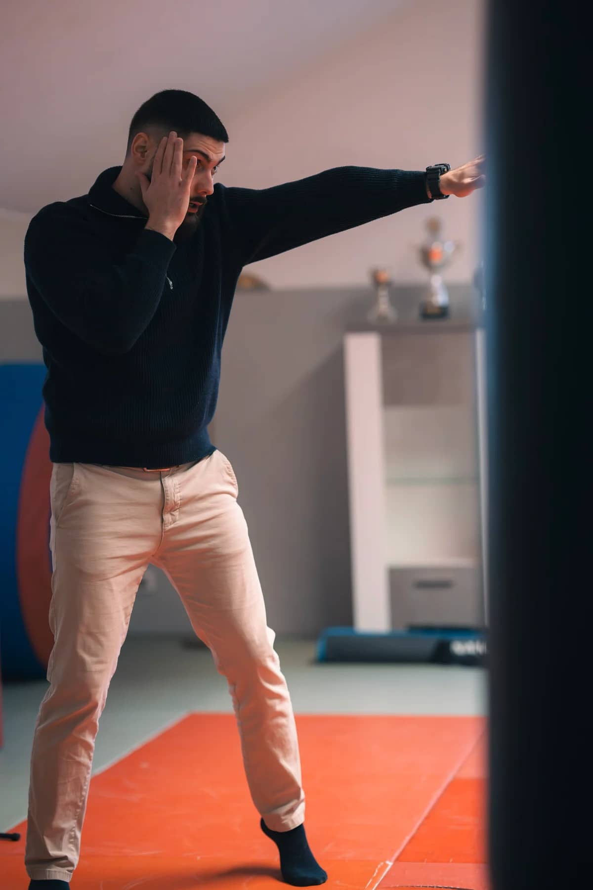 Ein Trainer demonstriert eine Schlagtechnik mit ausgestrecktem Arm und einer Hand am Kopf.