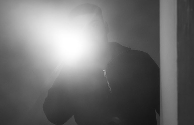 Mann mit Taschenlampe in einem dunklen, nebligen Raum.