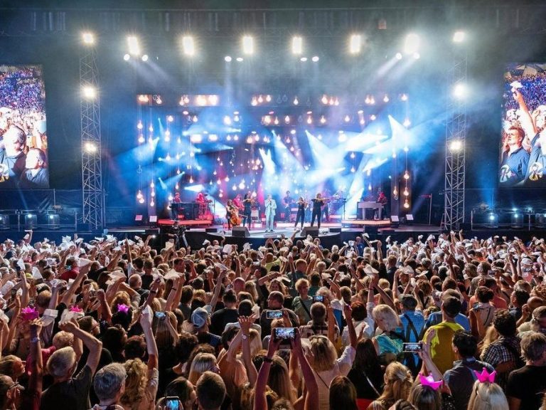 Großes Musikfestival mit einer begeisterten Menge und einer Lichtshow auf der Bühne.