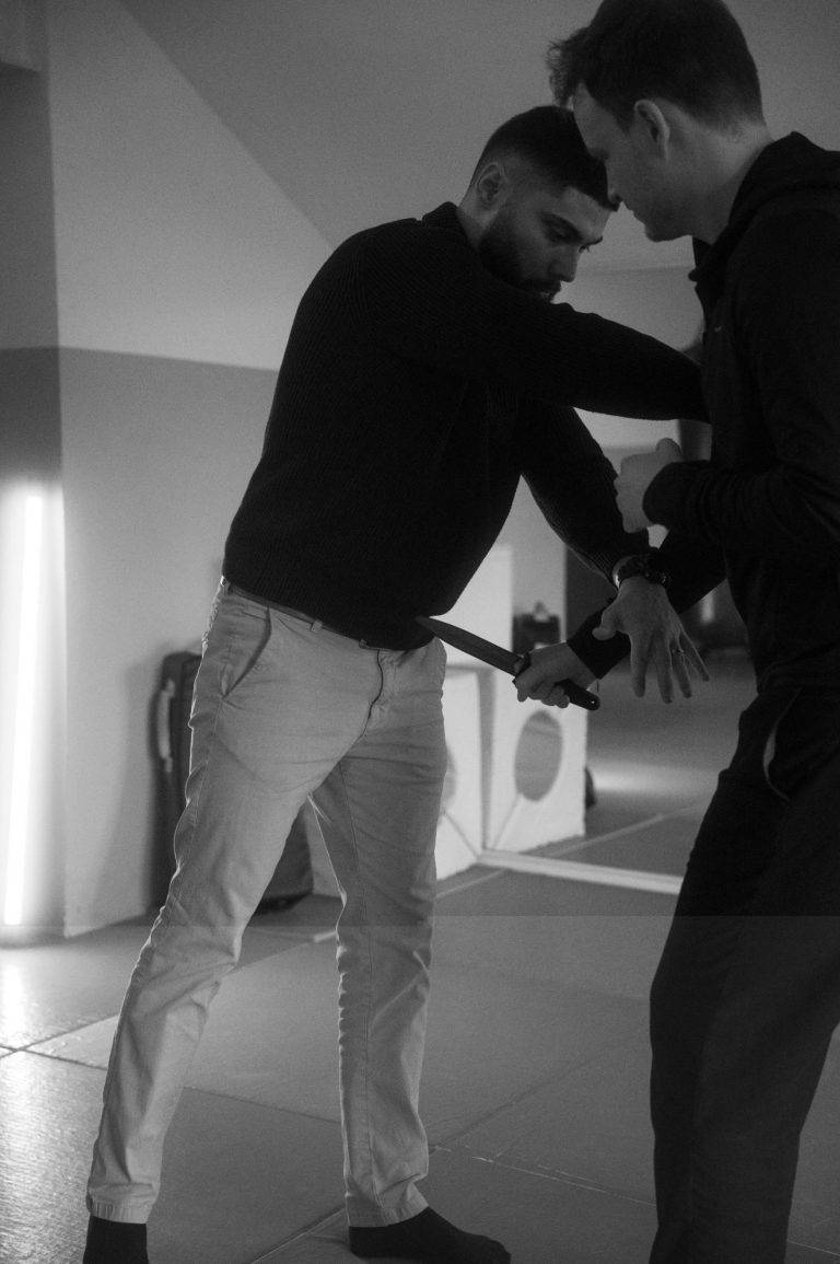 Zwei Personen üben eine Selbstvertechnik in einem Trainingsraum.