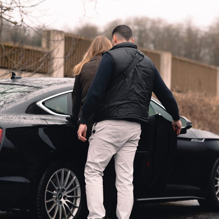 Ein Mann öffnet eine Tür für eine Frau, die neben einem schwarzen Auto steht.