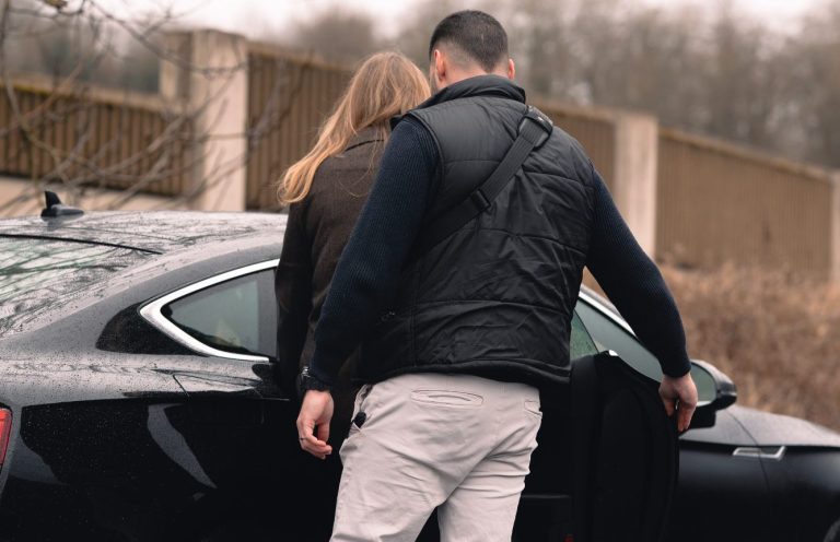 Zwei Personen stehen neben einem schwarzen Auto, während eine Person die Tür öffnet.
