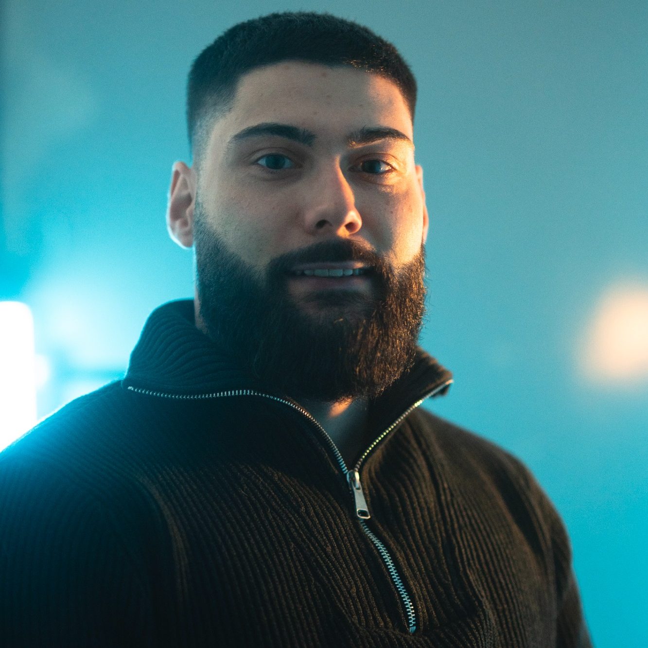 Mann mit kurzem Haar und Bart, lächelt vor hellem Hintergrund.