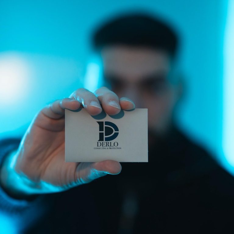 Eine Person hält eine Visitenkarte mit einem stilisierten Logo vor einem blauen Hintergrund.