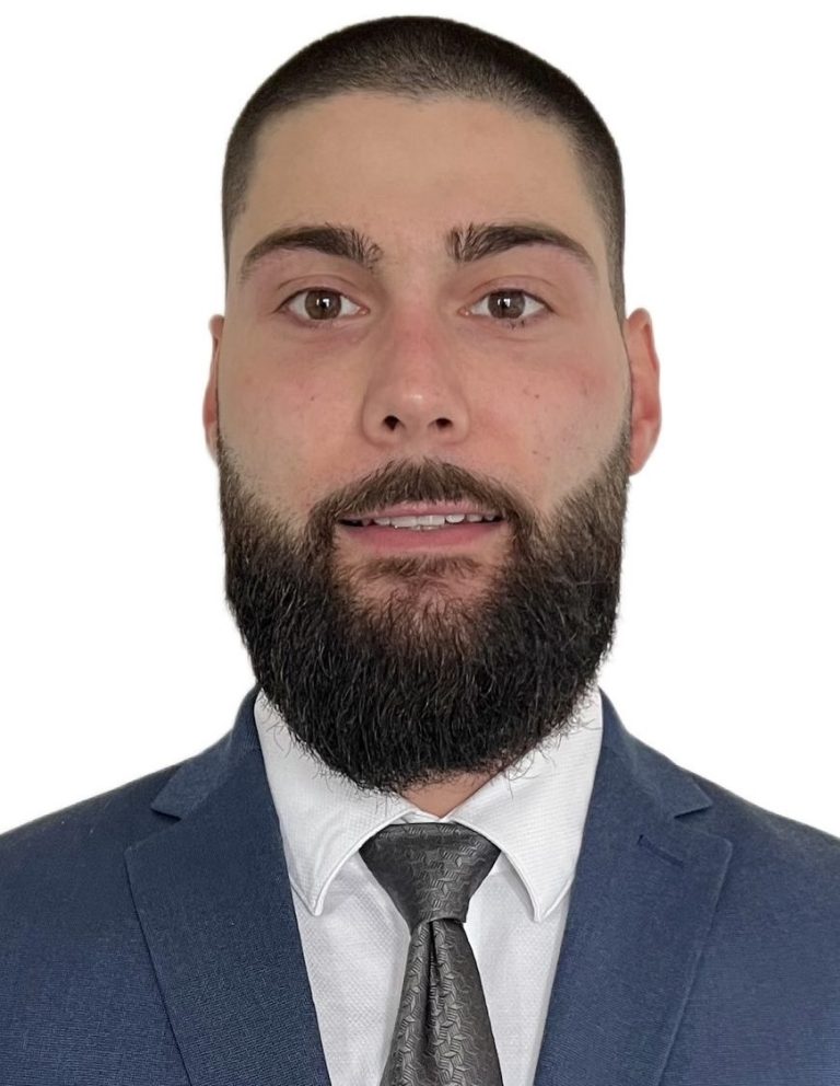 Mann mit kurzem Bart, Anzug und Krawatte, schaut direkt in die Kamera.