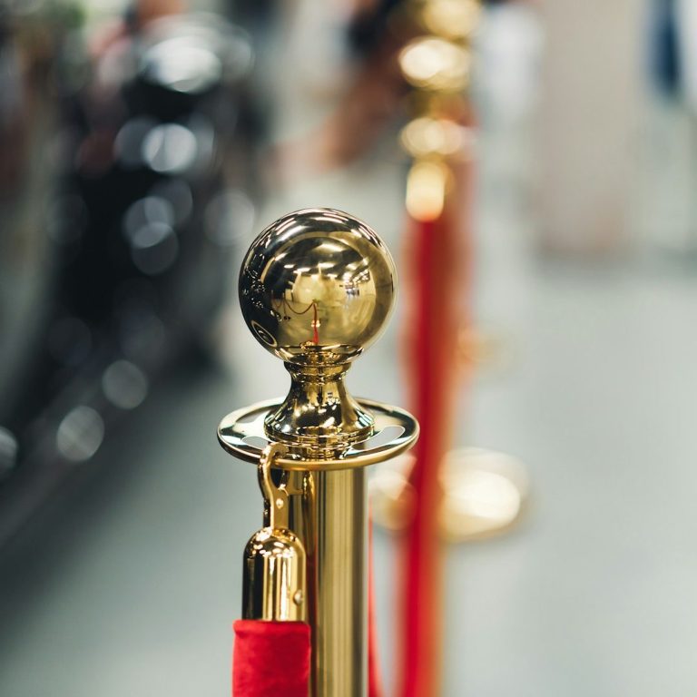 Goldene Absperrpfosten mit rotem Samtseil in einem Ausstellungsraum.