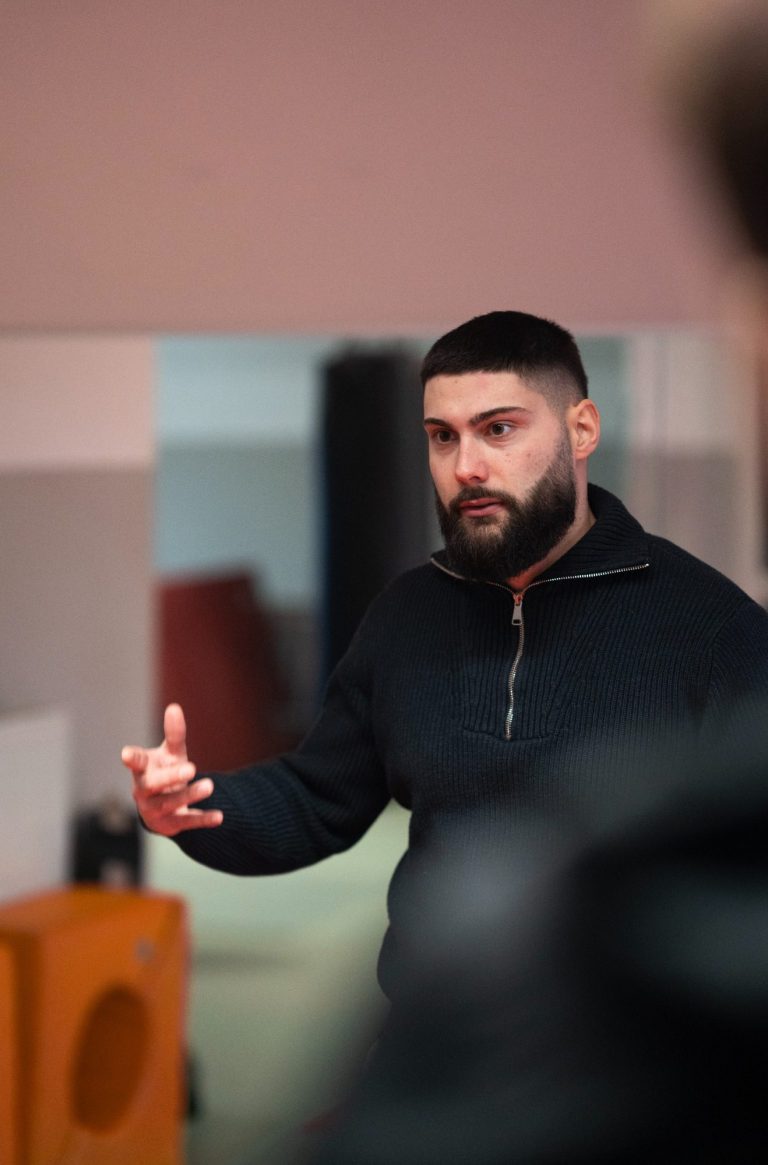 Ein Mann mit Bart erklärt etwas, während er auf einen kreativen Raum zeigt.