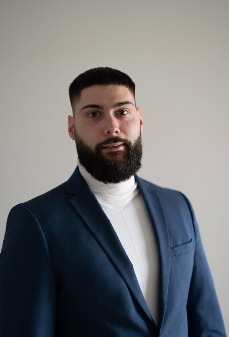 Mann mit Bart und gestylten Haaren in einem Anzug und Rollkragenpullover.