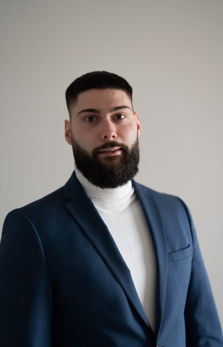 Mann mit Bart in Anzug und Rollkragenpullover vor neutralem Hintergrund.