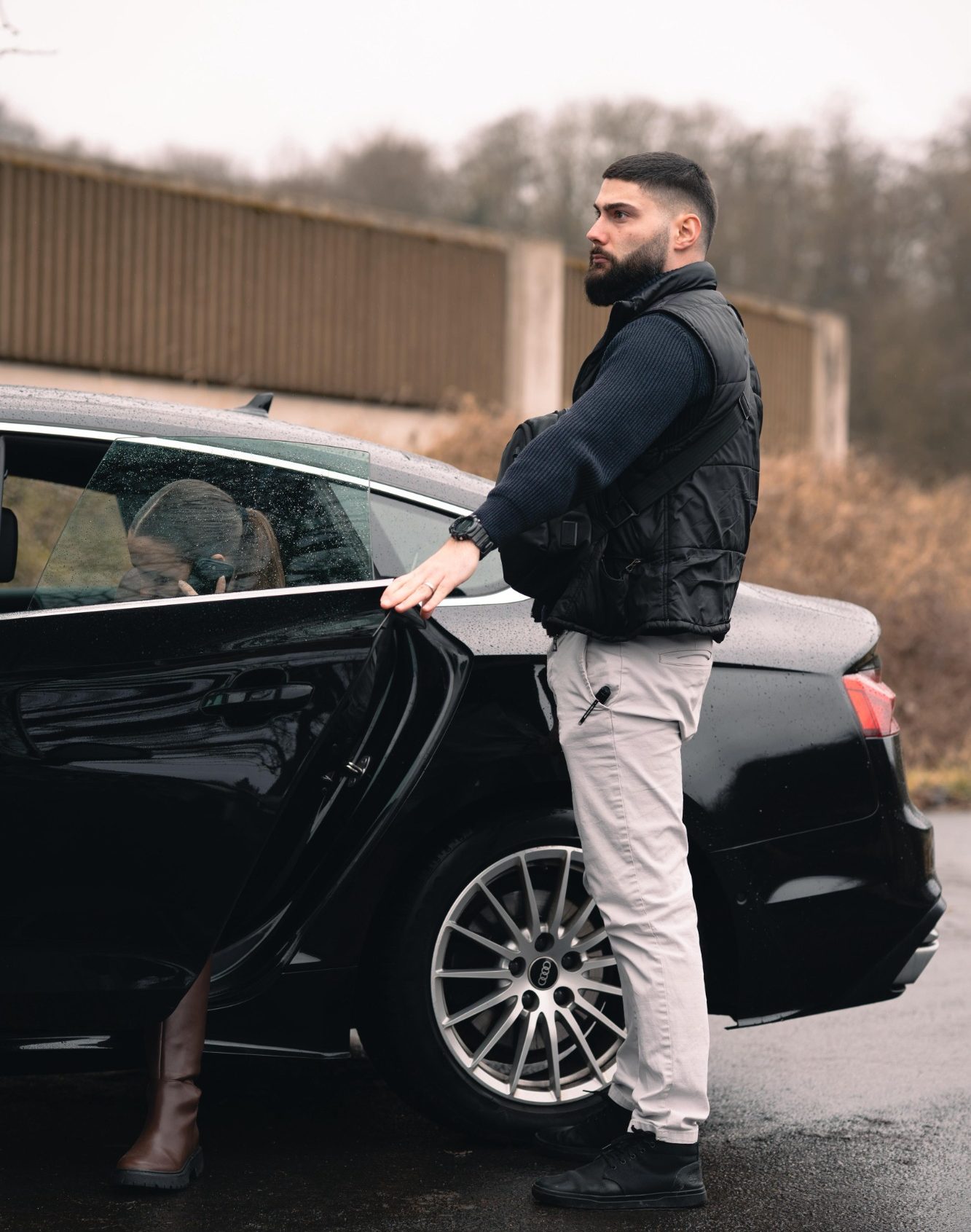 Mann im Parka steht neben einem schwarzen Auto und öffnet die Tür.