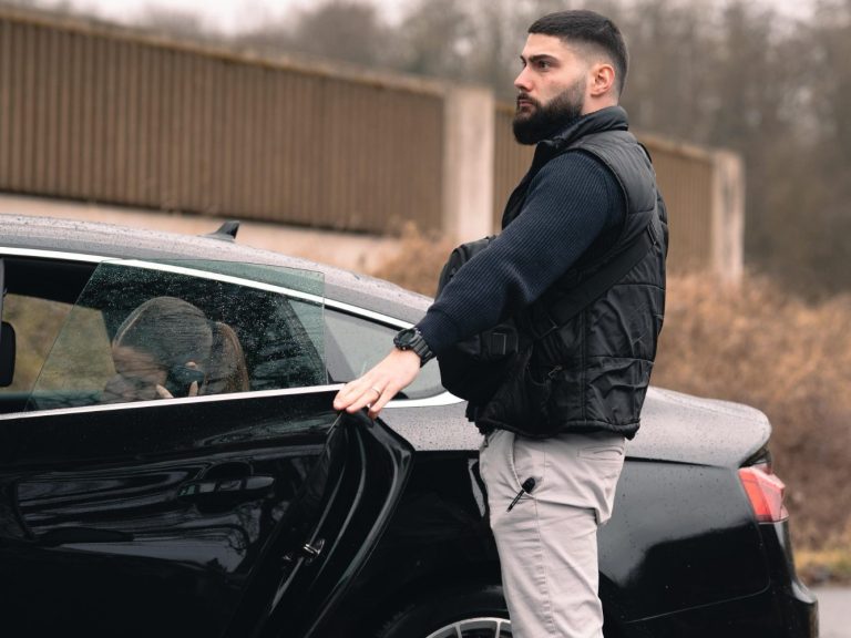 Mann in Jacke steht neben einem Auto und öffnet die Fahrertür.