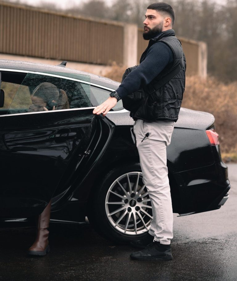 Ein Mann öffnet die Tür eines schwarzen Autos, während er auf einen schmalen Weg steht.