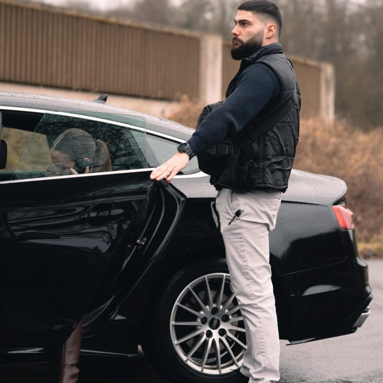Ein Mann steht an einem schwarzen Auto und öffnet die Tür.