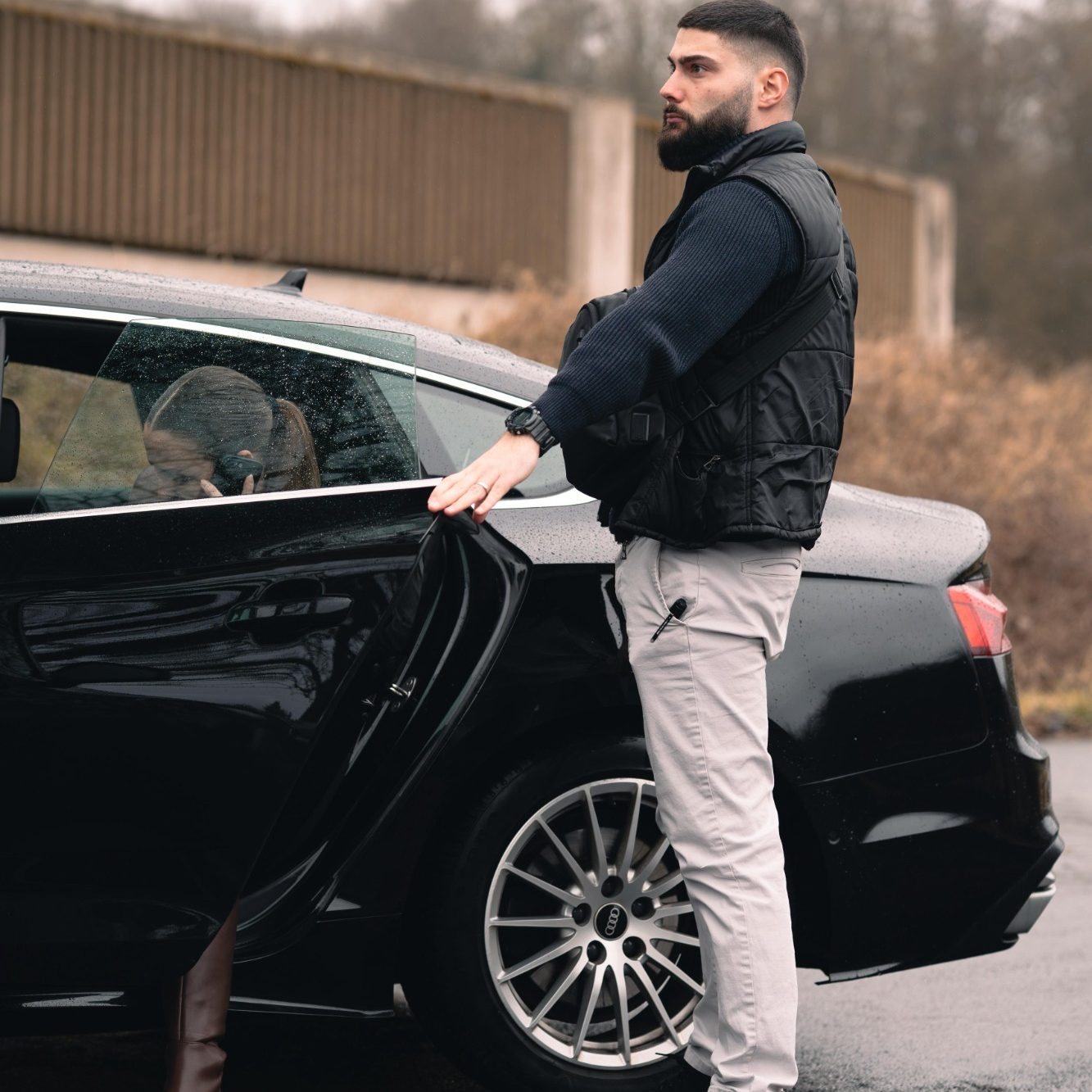 Mann in Weste öffnet die Tür eines schwarzen Autos.