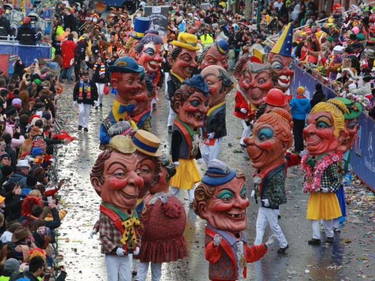 Bunte Umzugsgruppe mit großen Masken und fröhlichen Menschen in festlicher Kleidung.