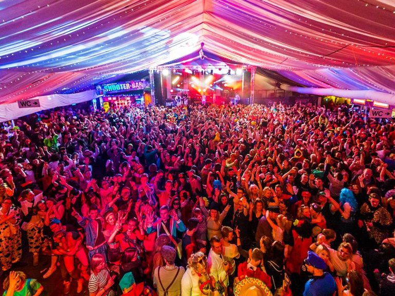 Voller Festzelt mit fröhlichen Menschen und bunten Lichtern, die tanzen und feiern.