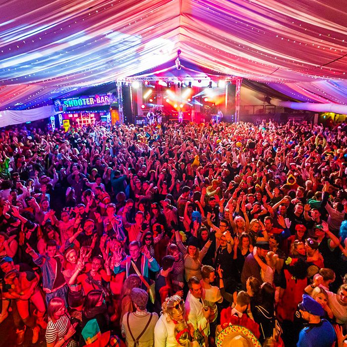 Große Menschenmenge feiert auf einem Festival unter festlich dekoriertem Zelt.