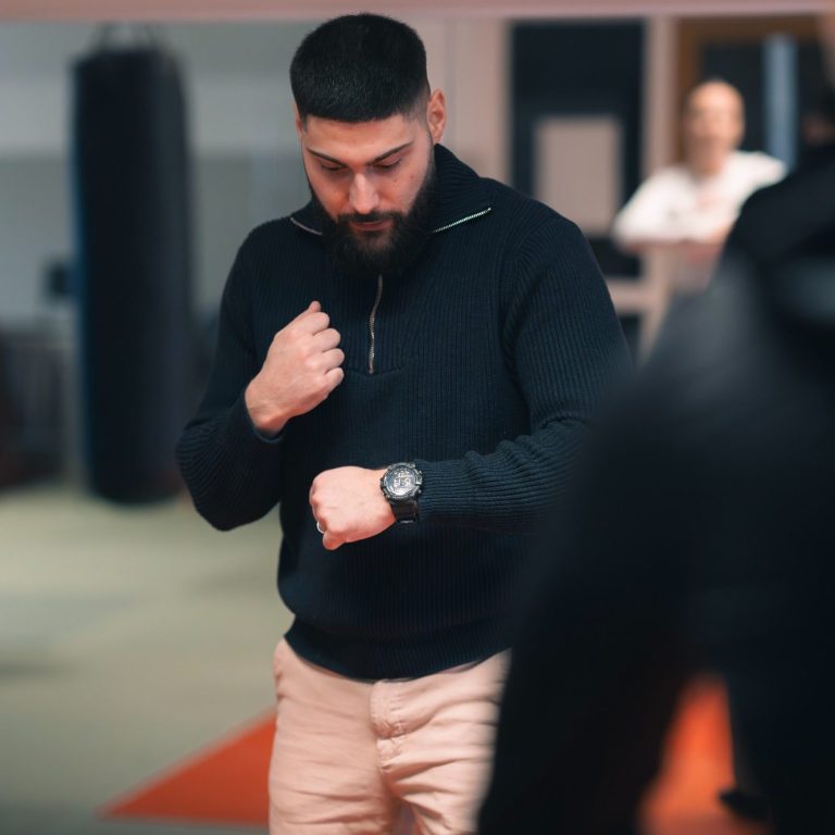 Mann im Trainingsanzug schaut auf seine Uhr in einem Fitnessstudio.