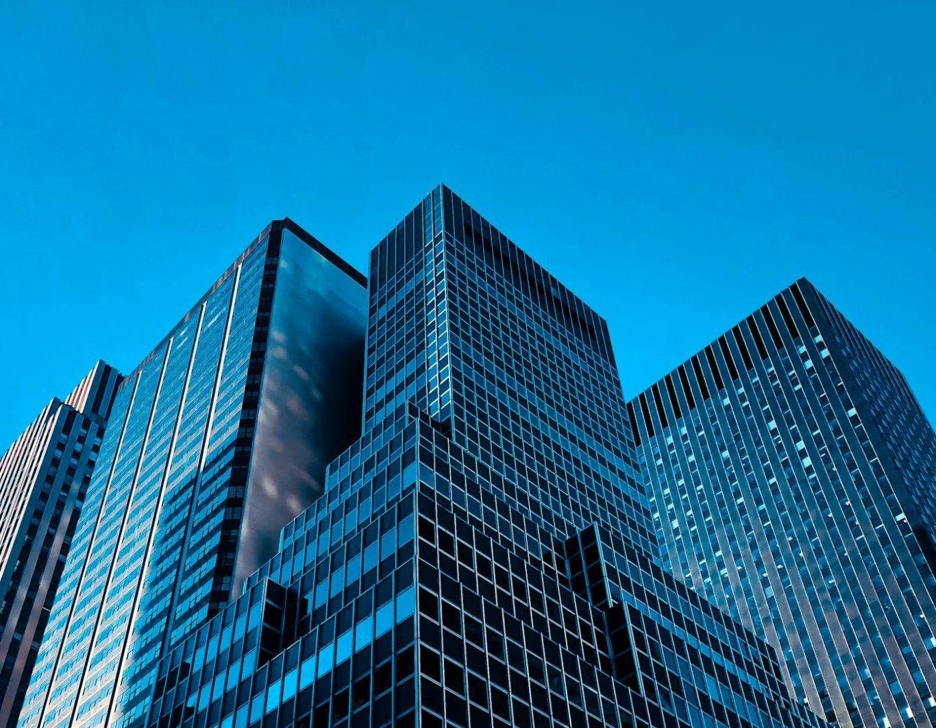 Hohe Bürogebäude mit modernen Glasfassaden vor blauem Himmel.